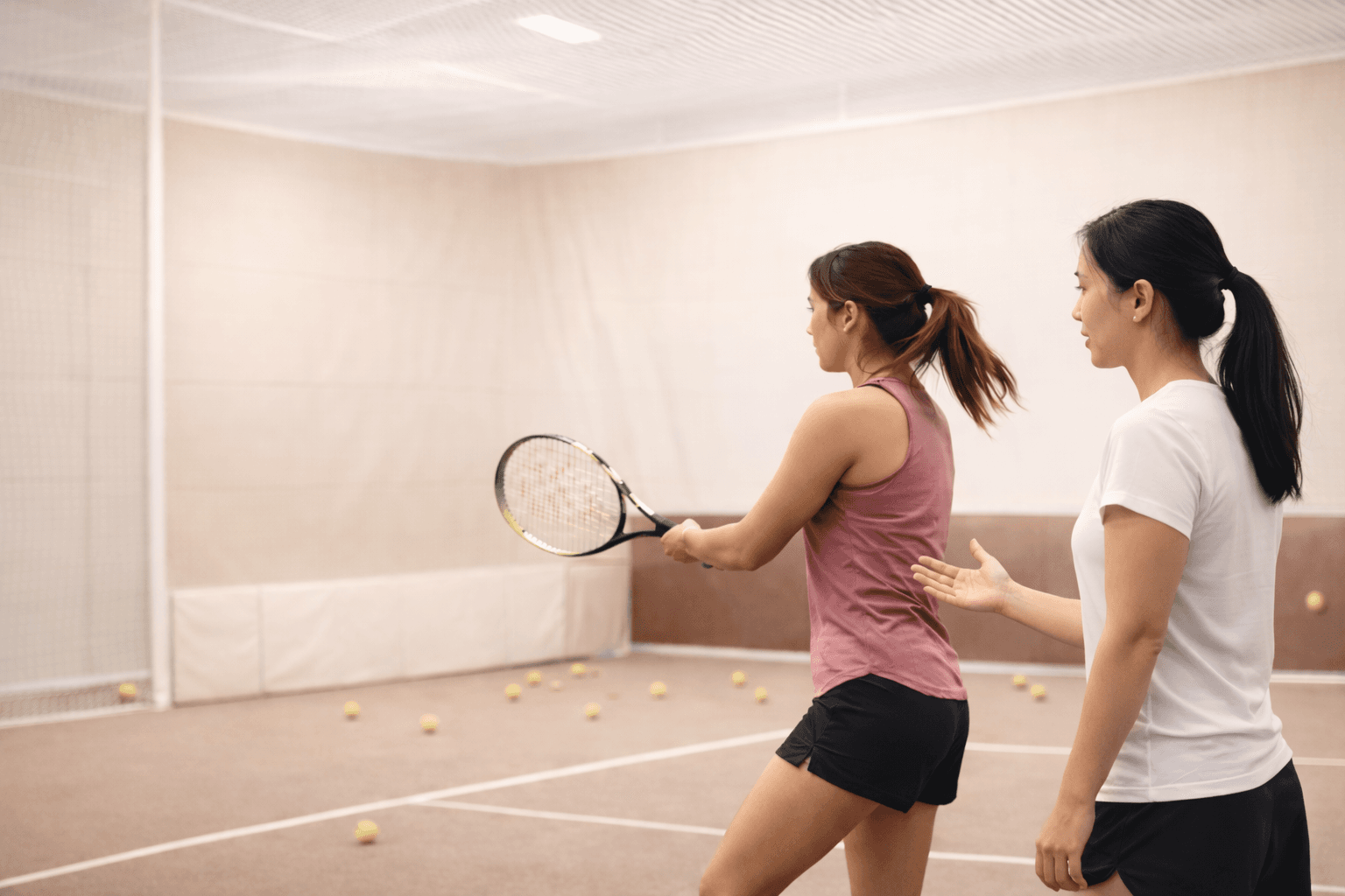 Two women training in an indoor tennis facility during a structured session